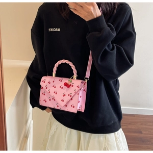 Detail of pink cherry print handbag with woven handle and cute cherry charms