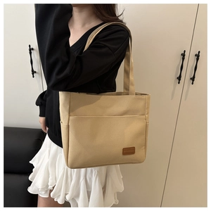 Detail of khaki canvas tote bag with front pocket and leather logo on a shoulder strap