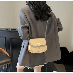 Detail of cream beige leather saddle bag with gold heart clasp and chain strap