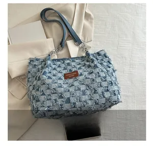 Detail view of denim plaid tote bag with frayed edges and brown leather patch