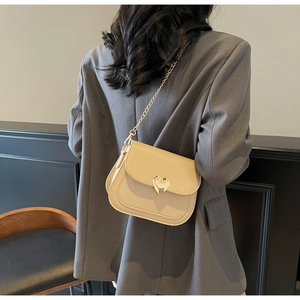 Detail of cream square bag with heart gold buckle and chain strap on a model