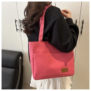 Close-up of deep pink canvas tote bag showing the front pocket and brown leather patch