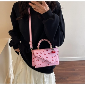 Detailed view of pink crossbody bag with red cherry prints and a twisted top handle