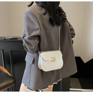 Silver glossy square crossbody bag with gold heart clasp worn over a grey blazer