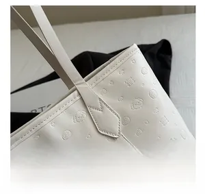 Close-up of white leather tote bag featuring cartoon embossed patterns and silver metal buckle