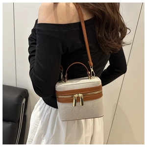 Detail of a chic box-shaped crossbody bag with gold zippers and textured beige fabric