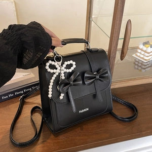 Chic black mini backpack with ribbon bows and pearl charm in a boutique setting