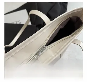 Close-up of top zipper closure on off-white faux leather tote bag with brown lining