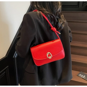 Detail of red leather shoulder bag with golden horseshoe buckle and knotted strap