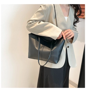 Detail of a large black leather tote bag with vertical stitching and embossed fashion logo