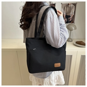 Detail of black canvas tote bag showing large front pocket and brown leather logo patch