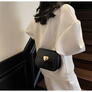 Detail of a black crossbody bag featuring a golden heart lock and fine chain strap
