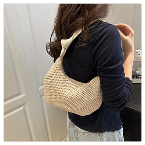 Close-up of a woven cream shoulder bag with a knotted strap detail on female model