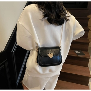 Detail of a black crossbody bag featuring a golden heart-shaped lock and chain strap