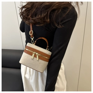 Detail of canvas vanity bag with brown leather trim and golden zipper on model