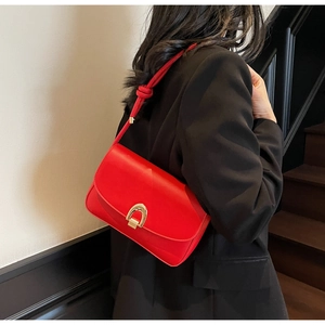 Detail of red minimalist underarm bag with gold horseshoe buckle on black blazer background