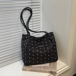 Minimalist black tote bag with white bow pattern and woven shoulder straps on a windowsill
