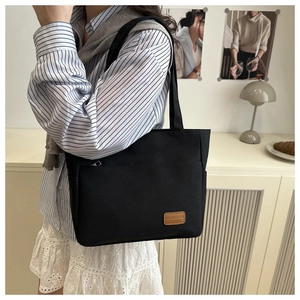 Detail of minimalist black canvas tote bag featuring front zipper pocket and leather brand tag