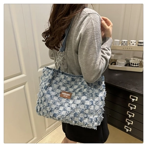 Detail of blue denim checkered tote bag featuring frayed edges and silver chain strap