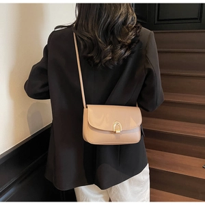 Detail of minimalist beige crossbody bag with gold arch buckle worn by a model