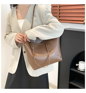 Detailed close-up of brown faux leather tote bag showing textured stitching and metal tag