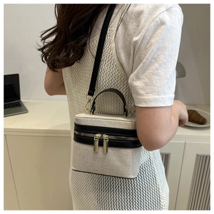 Detail of beige canvas crossbody bag with black leather trim and gold hardware accents
