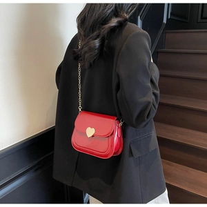 Close-up of red patent leather crossbody bag with gold heart-shaped buckle and chain strap