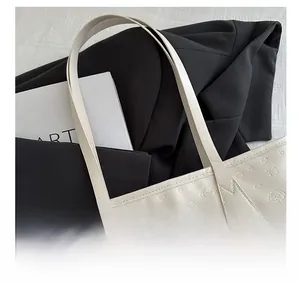 Detail of the reinforced wide shoulder strap and embossed pet pattern on the cream tote bag