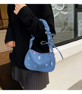 Close-up of denim shoulder bag featuring floral embroidery and ruched strap details