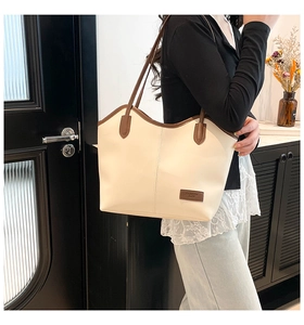 Shoulder view of a large cream tote bag with contrast brown trim and leather logo tag