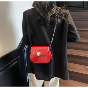 Close-up of red glossy saddle bag featuring a gold heart lock and thin chain strap
