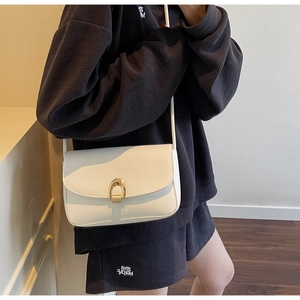 Detailed shot of white crossbody bag with golden horseshoe buckle on charcoal knitwear