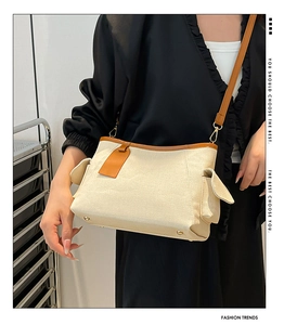 Dettaglio borsa a spalla in tela beige con finiture in pelle marrone e tasche laterali