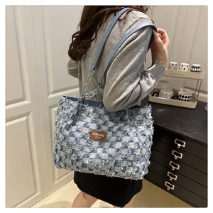 Macro detail of blue and white checkered denim tote with fringe edges and leather strap