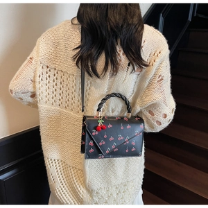 Detail of a black cherry print crossbody bag with woven handle and a 3D cherry charm