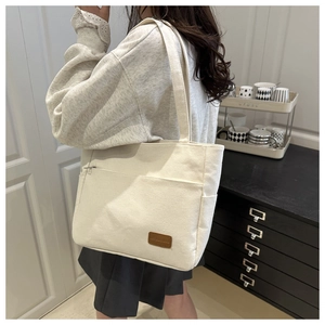 Detail of cream canvas tote bag showing the front zipper pocket and retro patch on the side