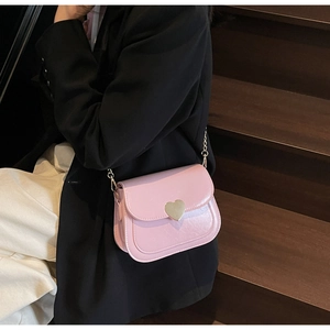 Detail view of the pink flap bag featuring a gold heart-shaped metal buckle and chain strap