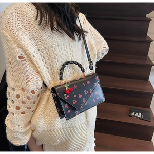 Detail of cherry print crossbody bag with woven handle shown on model in casual setting