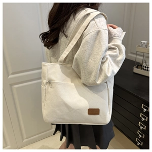 Detail of cream canvas tote bag showing side zipper pocket and brown leather logo patch
