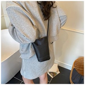 Detail of minimalist black pebbled leather cylinder crossbody bag shown on model