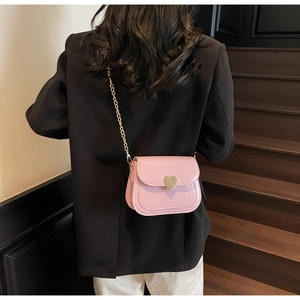 Close-up of a pink mini crossbody bag with a golden heart clasp on a black blazer