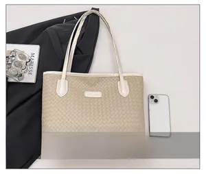 Detail of a beige woven tote bag with long handles and a branding plate in a lifestyle setup