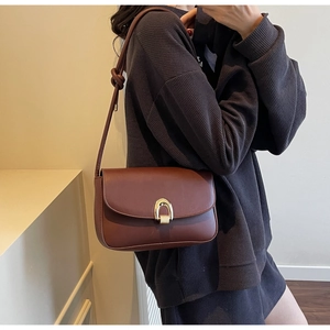 Close-up of brown leather shoulder bag featuring a golden horseshoe metallic clasp