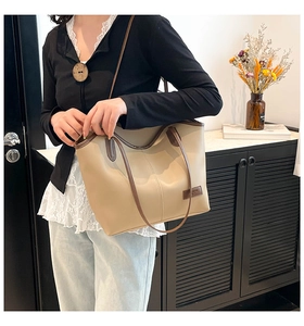 Detail of a beige minimalist tote bag showing contrast stitching and brown leather handles