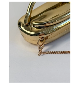 Detail of glossy gold shell-shaped evening clutch bag with metal chain strap