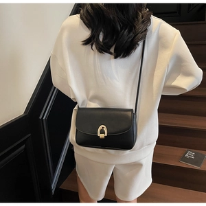 Detail of a black leather crossbody bag with a gold metal lock worn by a model