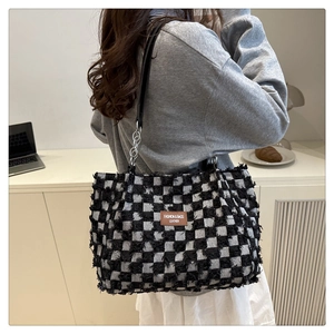 Detail of checkered tote bag with frayed edges, brown leather logo, and chain strap
