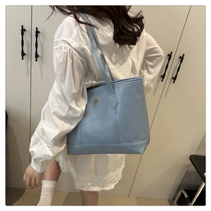 Detail view of light blue tote bag with embossed pattern and silver metal plaque