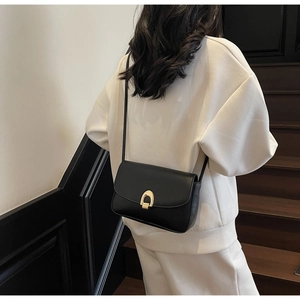 Classic black leather crossbody bag with a polished gold arch buckle on a white outfit