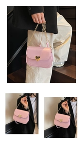 Detail of pink faux leather saddle bag featuring a gold heart clasp and metal chain strap